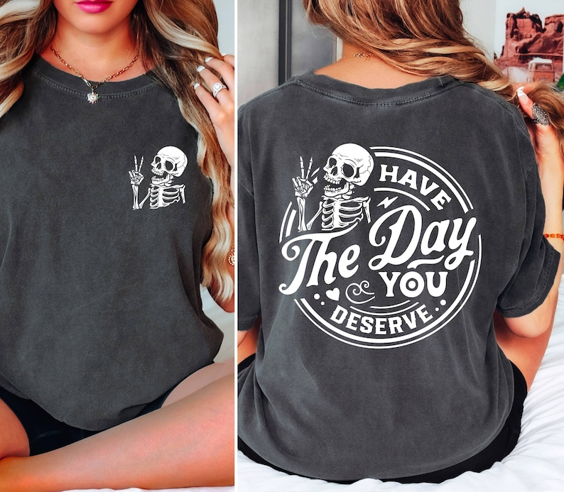 May include: A dark gray t-shirt with a white skeleton graphic on the front and a white circle graphic on the back that says "Have The Day You Deserve".