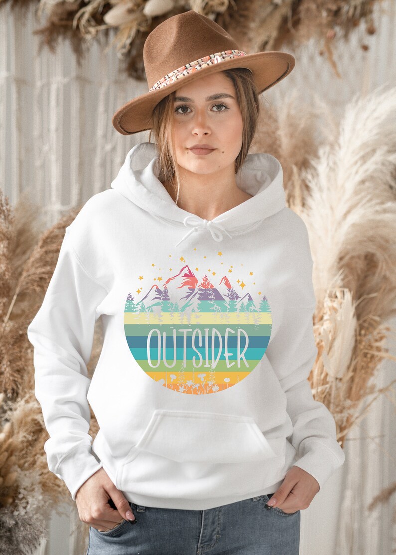 May include: White hoodie with a colorful mountain and forest graphic. The word "OUTSIDER" is printed in a bold font across the design. The hoodie has a drawstring hood and a front pocket.
