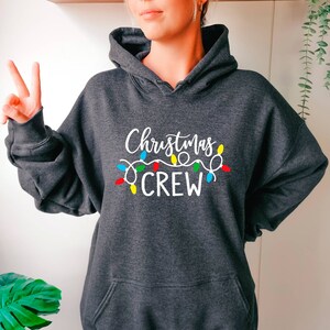 May include: Grey hooded sweatshirt with the text "Christmas Crew" in white, with a string of colourful Christmas lights above the text.