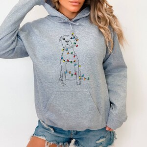 May include: A gray hooded sweatshirt with a white outline of a dog wearing colorful Christmas lights. The dog is sitting and looking forward.