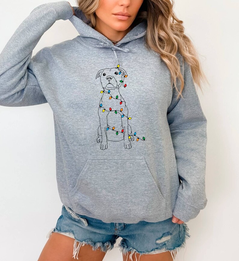 May include: A gray hooded sweatshirt with a white outline of a dog wearing colorful Christmas lights. The dog is sitting and looking forward.