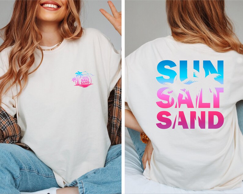 Pode incluir: Camiseta creme com um design tropical. A frente apresenta um pequeno gr&aacute;fico colorido de uma palmeira e as palavras "Sun Salt Sand". A parte de tr&aacute;s da camisa exibe as palavras "SUN SALT SAND" em letras grandes gradientes azuis e rosa.