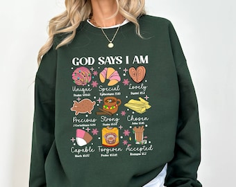 May include: Green sweatshirt with the text "GOD SAYS I AM" in white lettering. The sweatshirt features a variety of colorful illustrations of baked goods with bible verses and words like "Unique", "Special", "Lovely", "Precious", "Strong", "Chosen", "Capable", "Forgiven", and "Accepted".