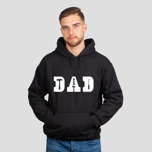 Puede incluir: Sudadera con capucha negra con un gr&aacute;fico blanco que dice "DAD" con herramientas incorporadas en las letras.