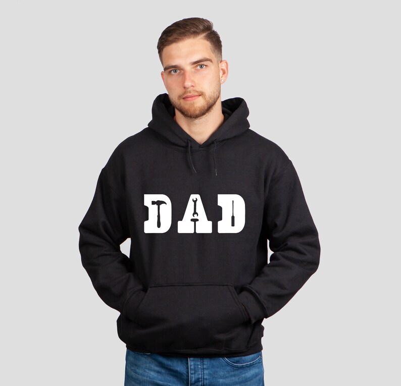 Puede incluir: Sudadera con capucha negra con un gr&aacute;fico blanco que dice "DAD" con herramientas incorporadas en las letras.