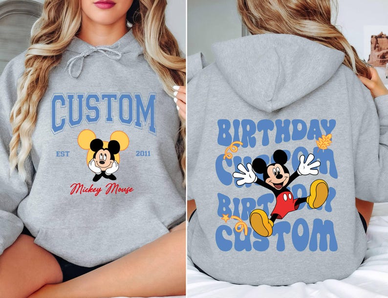 K&ouml;nnte beinhalten: Grauer Kapuzenpullover mit einem blauen und wei&szlig;en Aufdruck von Mickey Mouse. Der Aufdruck lautet "Custom" mit "Est 2011" und "Mickey Mouse" darunter. Die R&uuml;ckseite des Pullovers hat einen blauen und wei&szlig;en Aufdruck, der "Birthday Custom Birthday Custom" lautet.