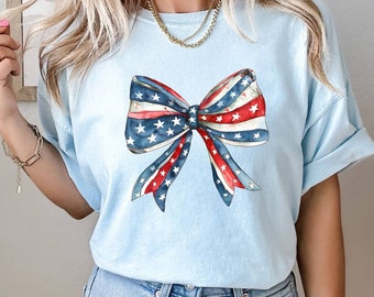May include: A light blue t-shirt with a red, white, and blue bow with stars printed on it.