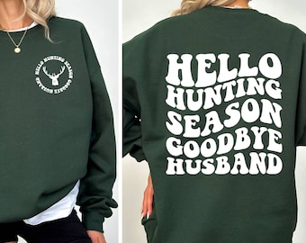 May include: Dark green sweatshirt with white text that reads "Hello Hunting Season Goodbye Husband" on the front and back. The front has a circular design with a deer silhouette. The back has the text in a stacked format.