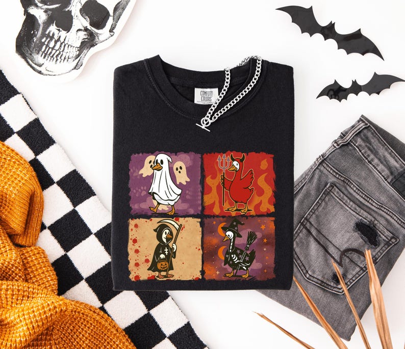 May include: Black t-shirt featuring a Halloween-themed graphic with four panels. Each panel depicts a duck dressed as a ghost, devil, grim reaper, and witch. The shirt is paired with gray jeans and a silver chain.