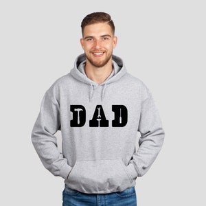 Puede incluir: Una sudadera con capucha gris con la palabra "DAD" impresa en negro. Las letras est&aacute;n formadas por herramientas, incluyendo un martillo, una llave inglesa y un destornillador.
