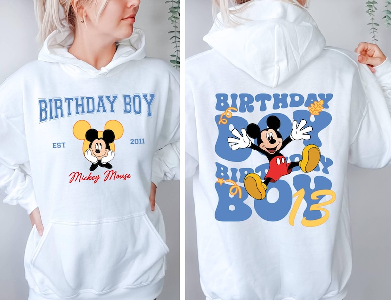 K&ouml;nnte beinhalten: Wei&szlig;er Hoodie mit einem blauen und gelben Motiv von Mickey Mouse auf der R&uuml;ckseite. Der Text "Birthday Boy" ist in blau und gelb auf der R&uuml;ckseite. Die Vorderseite des Hoodies hat ein kleineres Motiv von Mickey Mouse mit dem Text "Birthday Boy" in blau und gelb, "Est 2011" in schwarz und "Mickey Mouse" in rot.