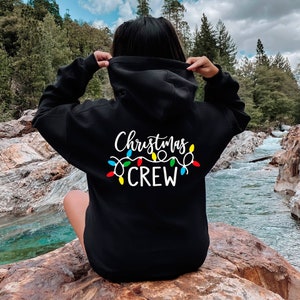 May include: Black hooded sweatshirt with white text that reads "Christmas Crew" and a string of colourful Christmas lights.