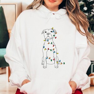 May include: White hoodie with a black line drawing of a dog with Christmas lights wrapped around it.