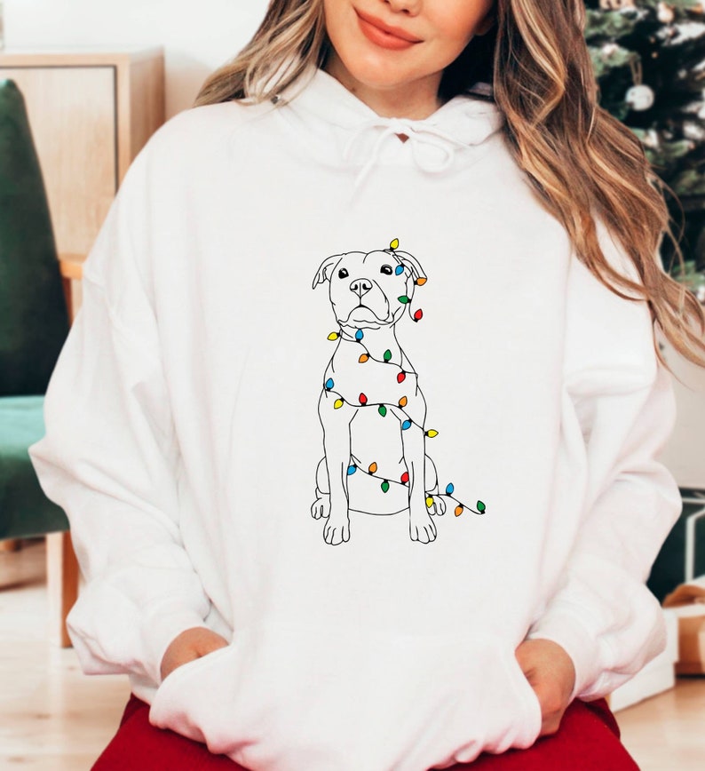 May include: White hoodie with a black line drawing of a dog with Christmas lights wrapped around it.