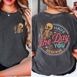 May include: Black t-shirt with a skeleton graphic on the front and a colorful graphic on the back that says "Have the Day You Deserve".