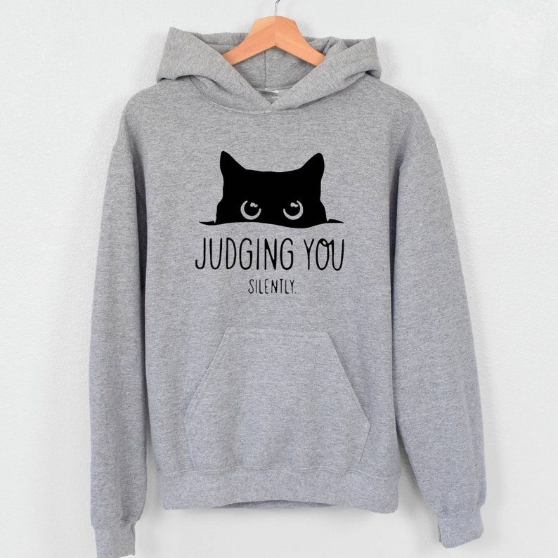 K&ouml;nnte beinhalten: Ein grauer Kapuzenpullover mit einer schwarzen Katze, die &uuml;ber den Rand schaut, und dem Text "JUDGING YOU SILENTLY."
