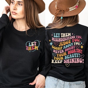 May include: Black sweatshirt with the text "LET THEM" inside a heart on the front. The back of the sweatshirt has the text "LET THEM MISUNDERSTAND YOU, JUDGE YOU, GOSSIP ABOUT YOU, NEVER DOUBT YOUR WORTH! YOUR BEAUTY! KEEP SHINING!"