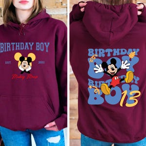 K&ouml;nnte beinhalten: Burgunderfarbener Hoodie mit einem Mickey-Mouse-Motiv und dem Text "Birthday Boy Est. 2011 Mickey Mouse". Die R&uuml;ckseite des Hoodies hat ein blaues Motiv mit dem Text "Birthday Boy Birthday Boy 13".