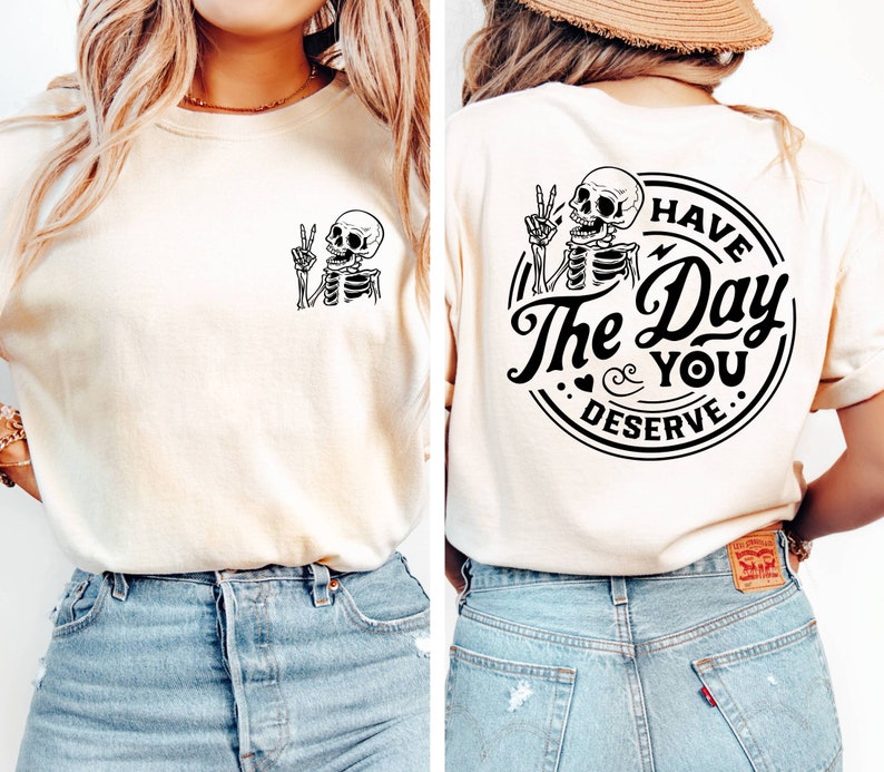 May include: A white t-shirt with a black skeleton graphic on the front and a black circle graphic on the back that says "Have the Day You Deserve".
