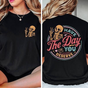 May include: Black t-shirt with a skeleton graphic and the text "Have the Day You Deserve" in a colorful circle.