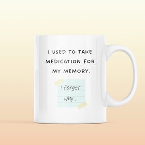 May include: White ceramic mug with a black text that reads "I used to take medication for my memory. I forget why..." with a yellow sticky note with blue lines and black text.