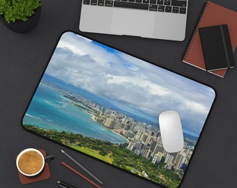 May include: A panoramic view of a city skyline with a beach and ocean in the foreground. The city is built on a peninsula with a green grassy area in the foreground. The sky is blue with white clouds.