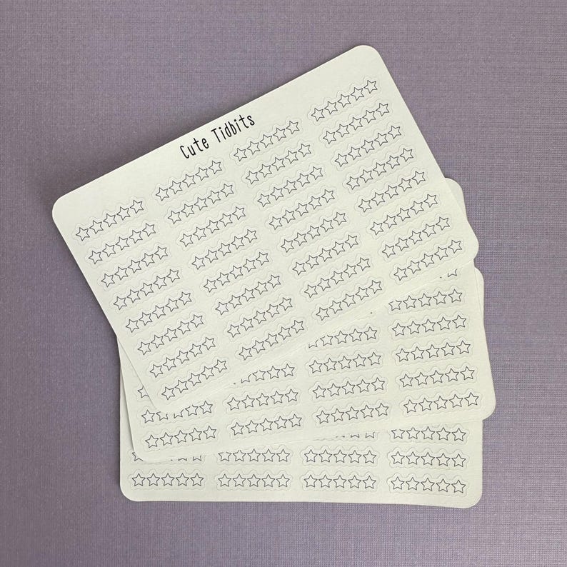 May include: A stack of white stickers with a light purple background. Each sticker has rows of outlined stars. The text "Cute Tidbits" is printed at the top of the top sticker. The stickers are likely for planning or crafting.