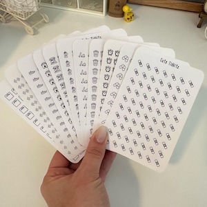 May include: A set of 10 sheets of white sticker paper with black outlines of various icons. The icons include a trash can, a clock, a coffee cup, a shoe, a lightbulb, a flower, and a bandage. The text "Cute Tidbits" is printed on one of the sheets.
