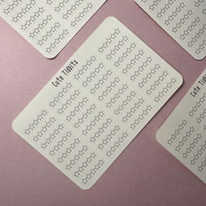 May include: Several white sticker sheets with rows of outlined star shapes. The text "Cute Tidbits" is printed on some of the sheets. The stickers are arranged on a light purple background.