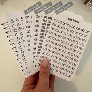 May include: A set of five sheets of black and white money themed stickers. The stickers are in four different styles, with the text "Cash - Style A", "Cash - Style B", "Cash - Style C", and "Cash - Style D" at the top of each sheet. The fifth sheet has the text "Cute Tidbits" at the top and features a grid of small money bag stickers.