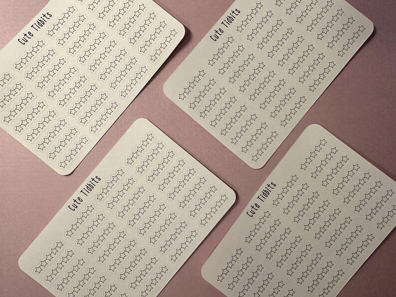 May include: Four white sticker sheets with rounded corners, each covered in rows of outlined star shapes. The text "Cute Tidbits" is printed in a handwritten style on each sheet. The stickers are arranged on a pink surface.