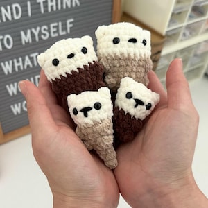 May include: Four handmade crochet bear figures in varying sizes, held in open hands. The bears are white, brown, and tan, with black eyes and noses. The background includes a letter board with the text "AND I THINK TO MYSELF WHAT A WONDERFUL WORLD".