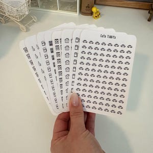 May include: A set of eight sheets of white sticker paper with black outlines of various icons. The icons include houses, cameras, and cars. The text "Cute Tidbits" is printed on the top of one sheet.