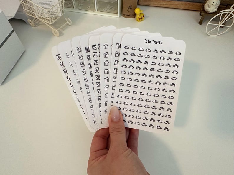 May include: A set of eight sheets of white sticker paper with black outlines of various icons. The icons include houses, cameras, and cars. The text "Cute Tidbits" is printed on the top of one sheet.