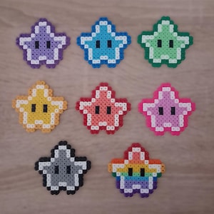 Könnte beinhalten: Acht sternförmige Figuren aus kleinen Kunststoffperlen, die in einem Raster angeordnet sind. Die Sterne haben verschiedene Farben wie Lila, Blau, Grün, Gelb, Pink, Magenta, Grau und ein Regenbogenmuster, jeweils mit zwei schwarzen Augen.
