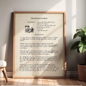 Könnte beinhalten: Ein gerahmter Druck mit einem Rezept für Shortbread-Cookies im Vintage-Stil. Der Text ist schwarz auf cremefarbenem Hintergrund, mit einer kleinen Illustration eines Glases und Teetassen. Eine Topfpflanze steht neben dem Rahmen.