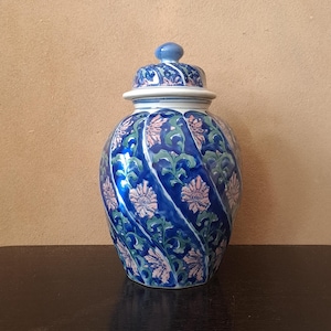 May include: A blue and white ceramic jar with a lid, decorated with pink and green floral patterns. The jar has a swirling design.