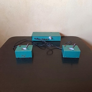 May include: A vintage green electronic game with two controllers and a central control unit. The controllers have black handles and are connected to the control unit by wires.