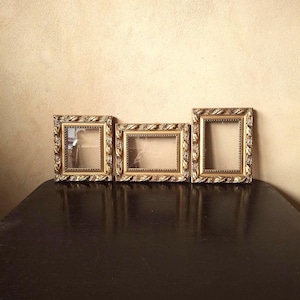 Un trío de marcos de fotos de madera pequeños y ornamentados de color dorado con un motivo natural idéntico.