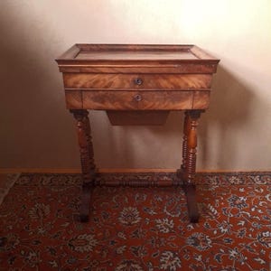 Könnte beinhalten: Ein Holztisch mit zwei Schubladen und gedrehten Beinen. Der Tisch hat eine dunkelbraune Oberfläche und steht auf einem roten Teppich mit Muster.