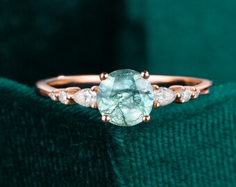May include: A rose gold ring with a round, green gemstone surrounded by smaller, clear gemstones.