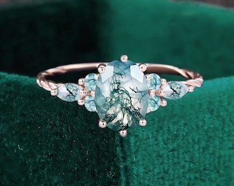 May include: A rose gold ring with a large oval green moss agate gemstone surrounded by smaller clear gemstones.