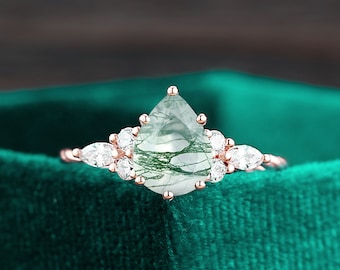 May include: A pear-shaped green moss agate engagement ring set in rose gold with a halo of smaller clear diamonds.