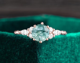 May include: A rose gold engagement ring with a green moss agate gemstone surrounded by smaller diamonds. The ring is set in a delicate band with a floral design.