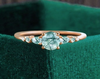 May include: A rose gold ring with a round green gemstone surrounded by smaller pear-shaped gemstones.