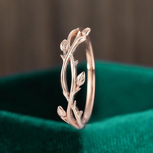 Puede incluir: Un delicado anillo de oro rosa con un diseño de rama con hojas. El anillo es una pieza de joyería simple y elegante.