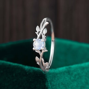 Op de afbeelding: Een zilveren ring met een delicaat takontwerp en een heldere edelsteen. De ring ligt op een groene fluwelen achtergrond.