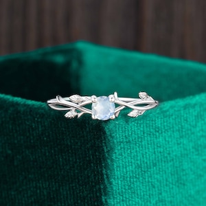 Op de afbeelding: Een zilveren ring met een delicaat takontwerp en een heldere ovale edelsteen. De ring ligt op een groene fluwelen achtergrond.