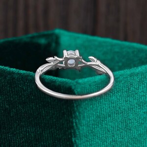 Op de afbeelding: Een zilveren ring met een delicaat takontwerp en een heldere edelsteen in het midden. De ring ligt op een groene fluwelen achtergrond.
