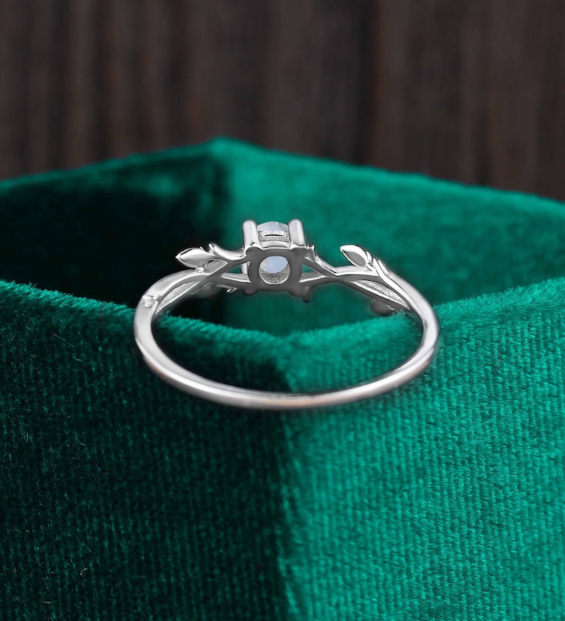 Op de afbeelding: Een zilveren ring met een delicaat takontwerp en een heldere edelsteen in het midden. De ring ligt op een groene fluwelen achtergrond.